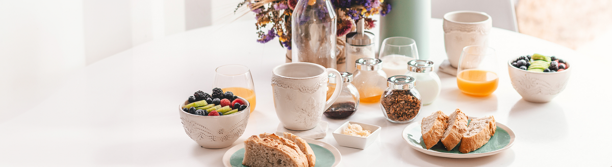 Gedeckter Frühstückstisch mit Brot, Obstschalen, Joghurt, Orangensaft und Müsli