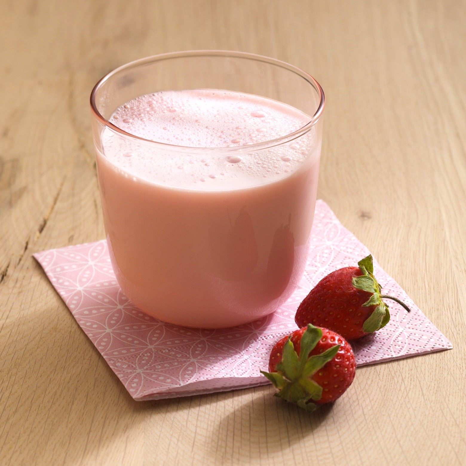 Ein Glas rosa Erdbeermilch und frische Erdbeeren auf einer gemusterten Serviette sind ein köstlicher Genuss, perfekt für das Gewichtsmanagement mit dem Precon 3-Monats-Mega-Vorrats-Paket CH.