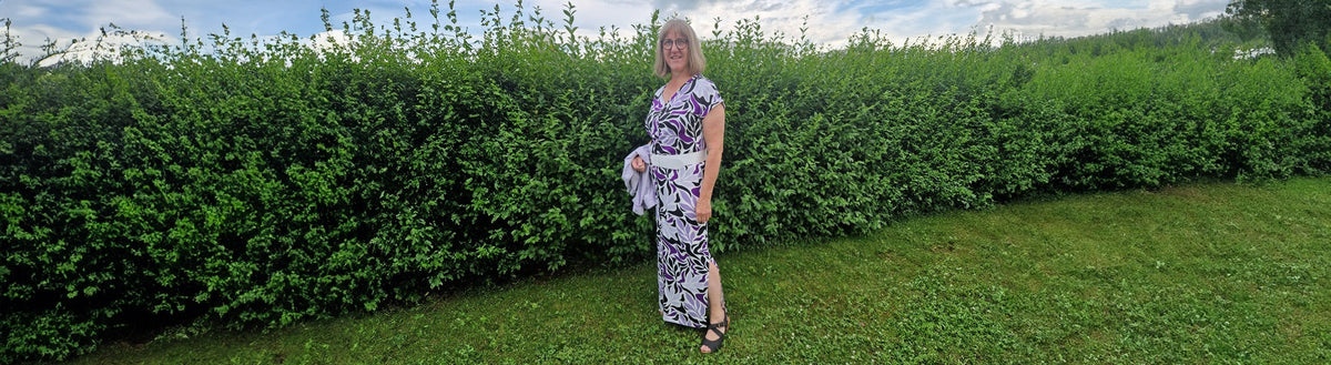 Rita (59) nach ihrer Gewichtsabnahme mit Precon, im gemusterten Kleid vor einer grünen Hecke