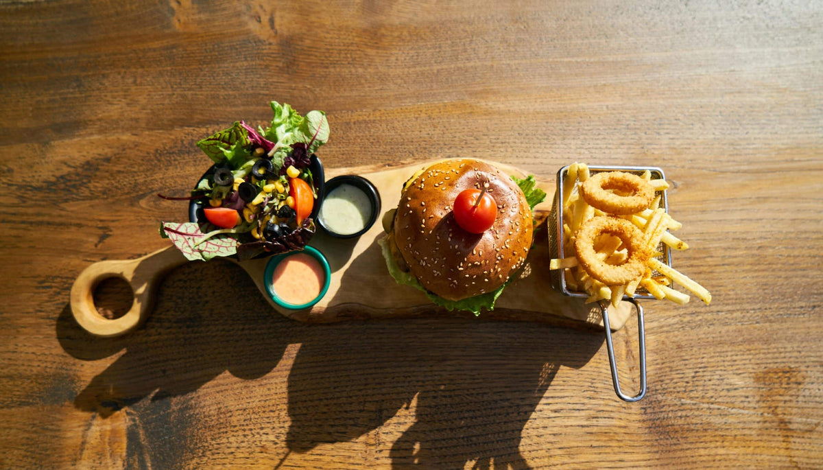 Burger mit Pommes, Zwiebelringen und Salat auf einem Holzbrett, von oben fotografiert