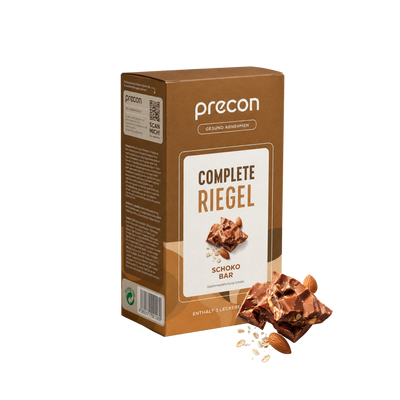 Eine braune Verpackung von „Complete Riegel ChocoBar“ der Anona GmbH, auf deren Vorderseite Schokoladenstückchen, Haferflocken und Mandeln abgebildet sind. Die Verpackung mit deutscher Beschriftung ist vor einem weißen Hintergrund abgebildet.